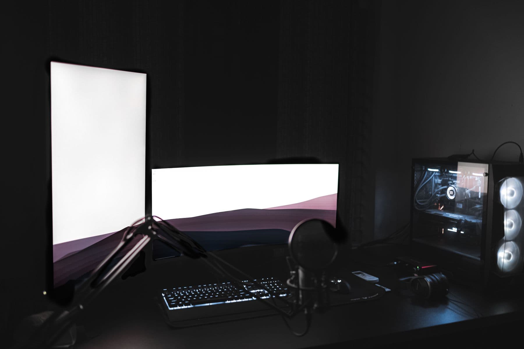 Dark creative workstation with dual monitors, keyboard, microphone, and desktop computer